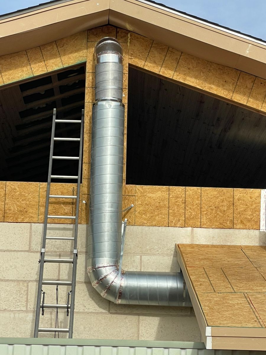 Metal ductwork extending from a building under construction, with a ladder leaning against it.