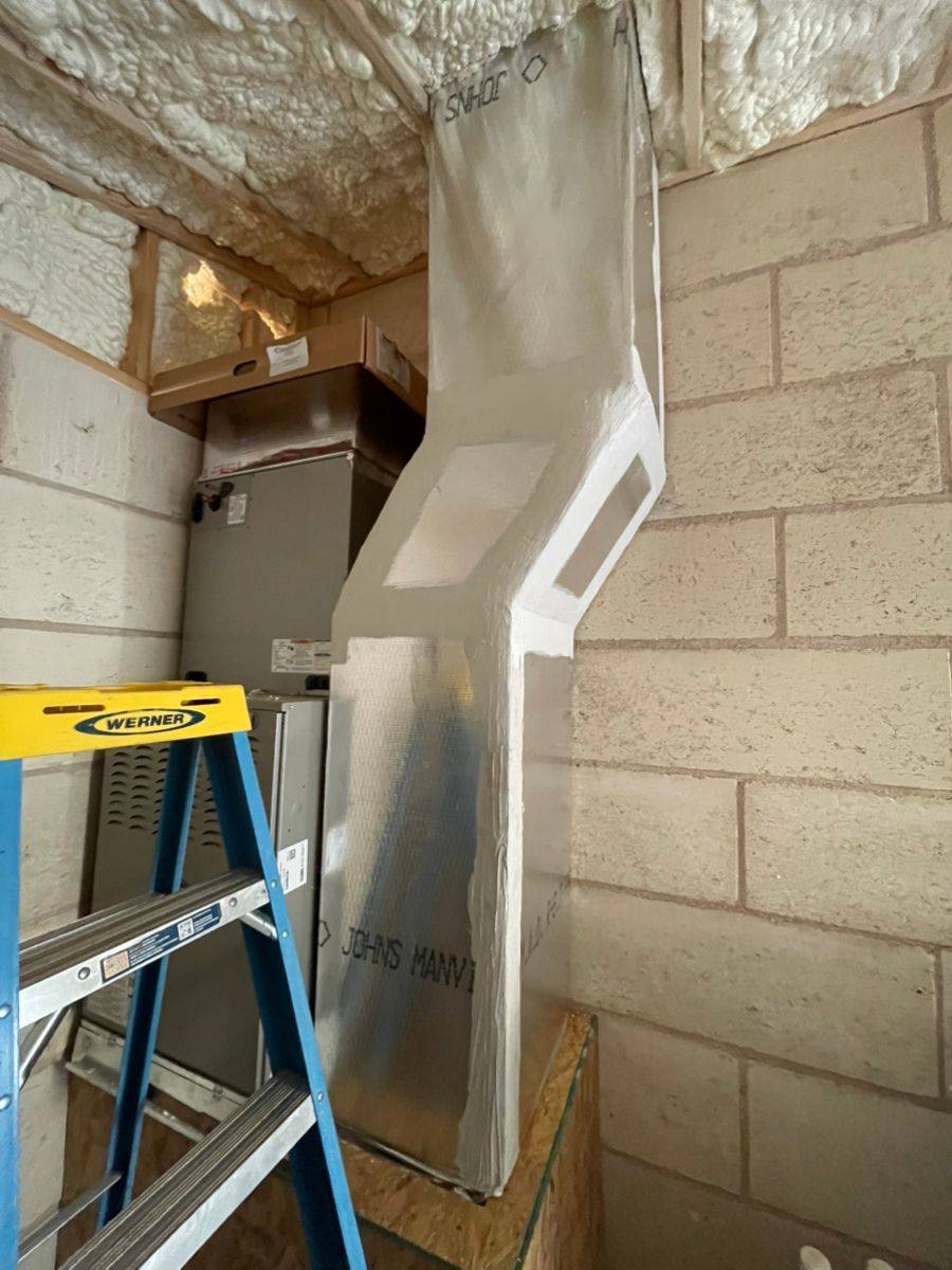 HVAC ductwork installation in a basement with a ladder next to the unit.