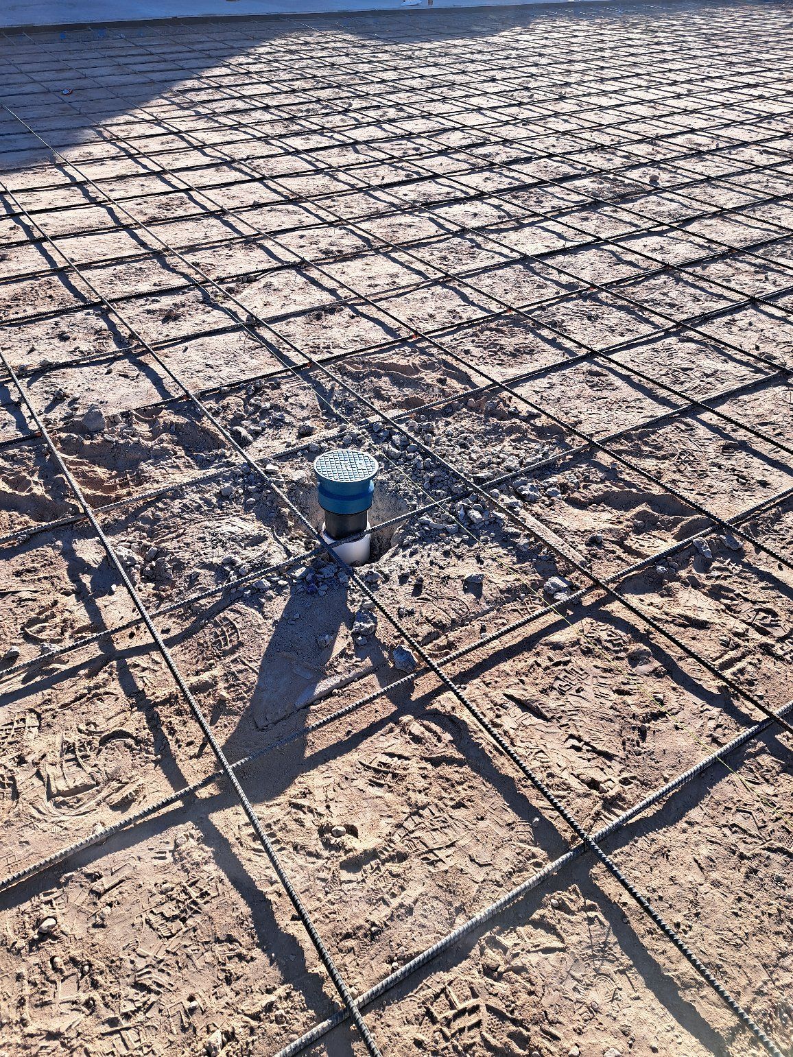 Reinforced metal grid over dirt with plumbing pipe, ready for concrete pour.