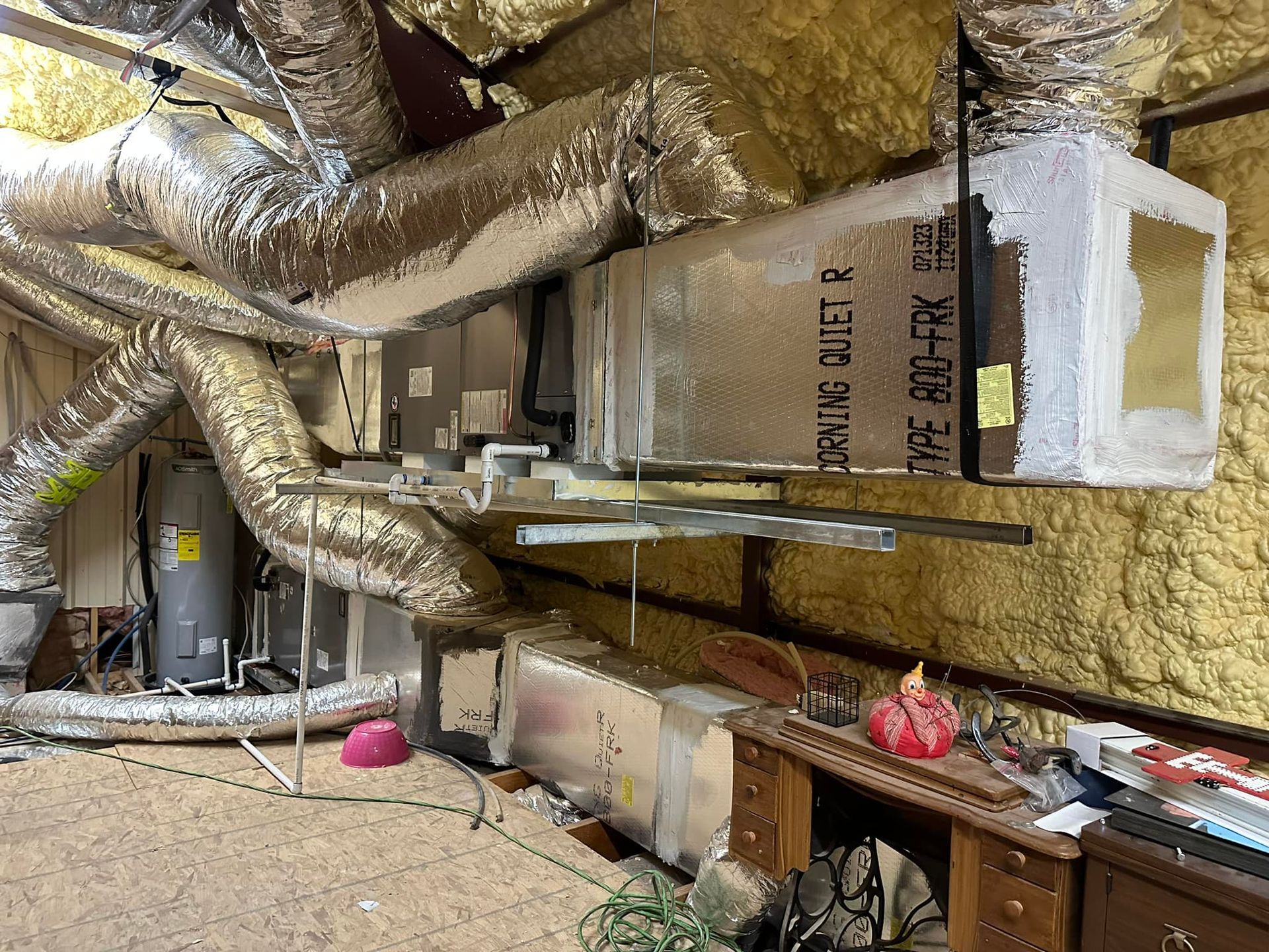 Insulated attic with exposed HVAC ducts, vents, and stored items along the floor.