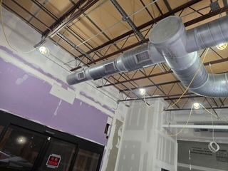 Indoor construction ceiling with exposed ductwork, hanging lights, and purple walls above a storefront.
