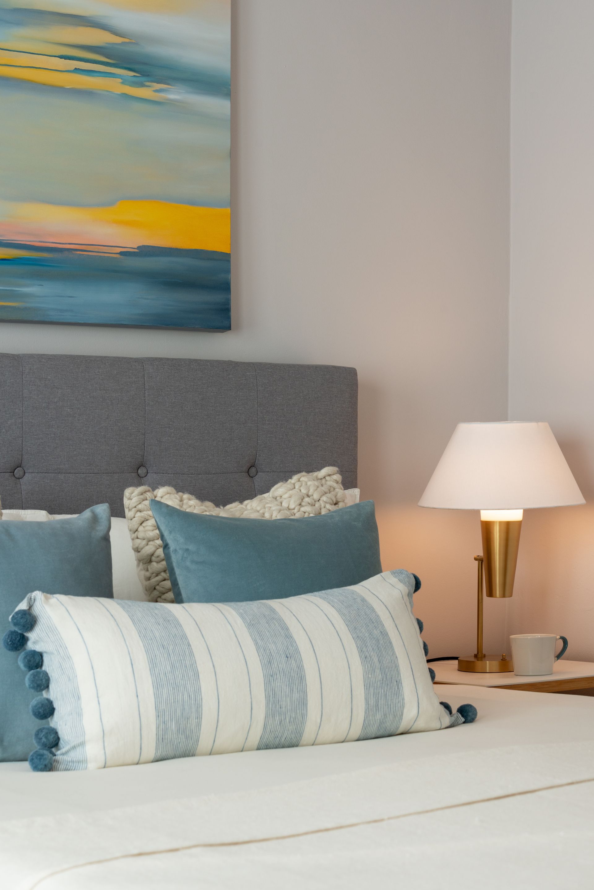 A bedroom with a bed , lamp , and painting on the wall.