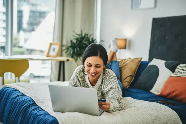 A woman is laying on a bed using a laptop computer.