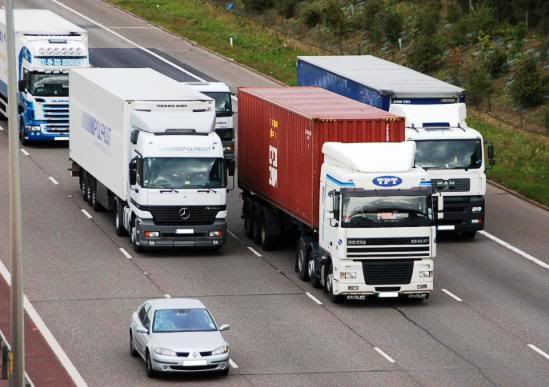 A row of trucks are driving down a highway with a car in the foreground