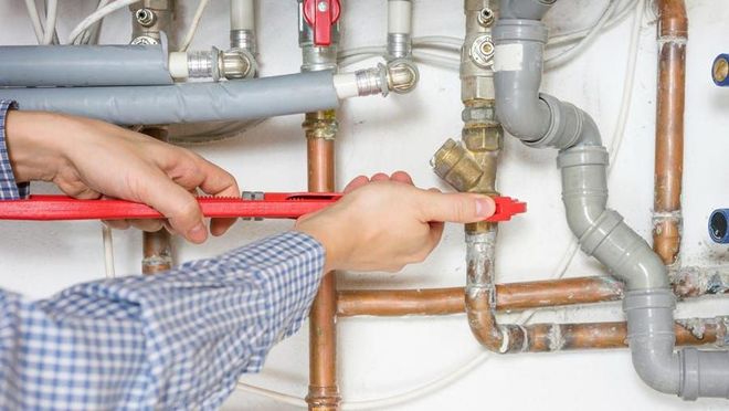 A plumber is fixing a pipe with a wrench.