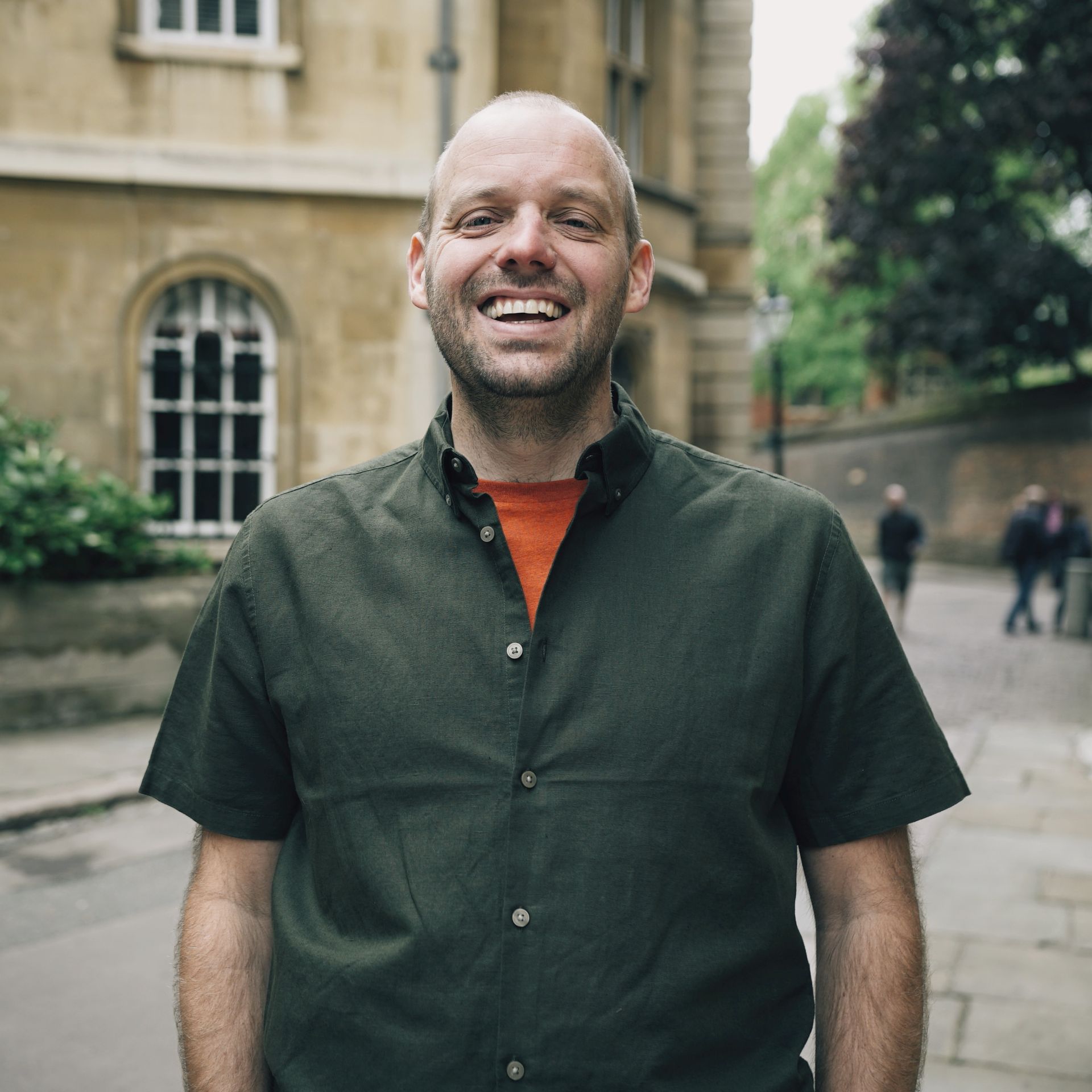 A man in a green shirt is smiling in front of a building