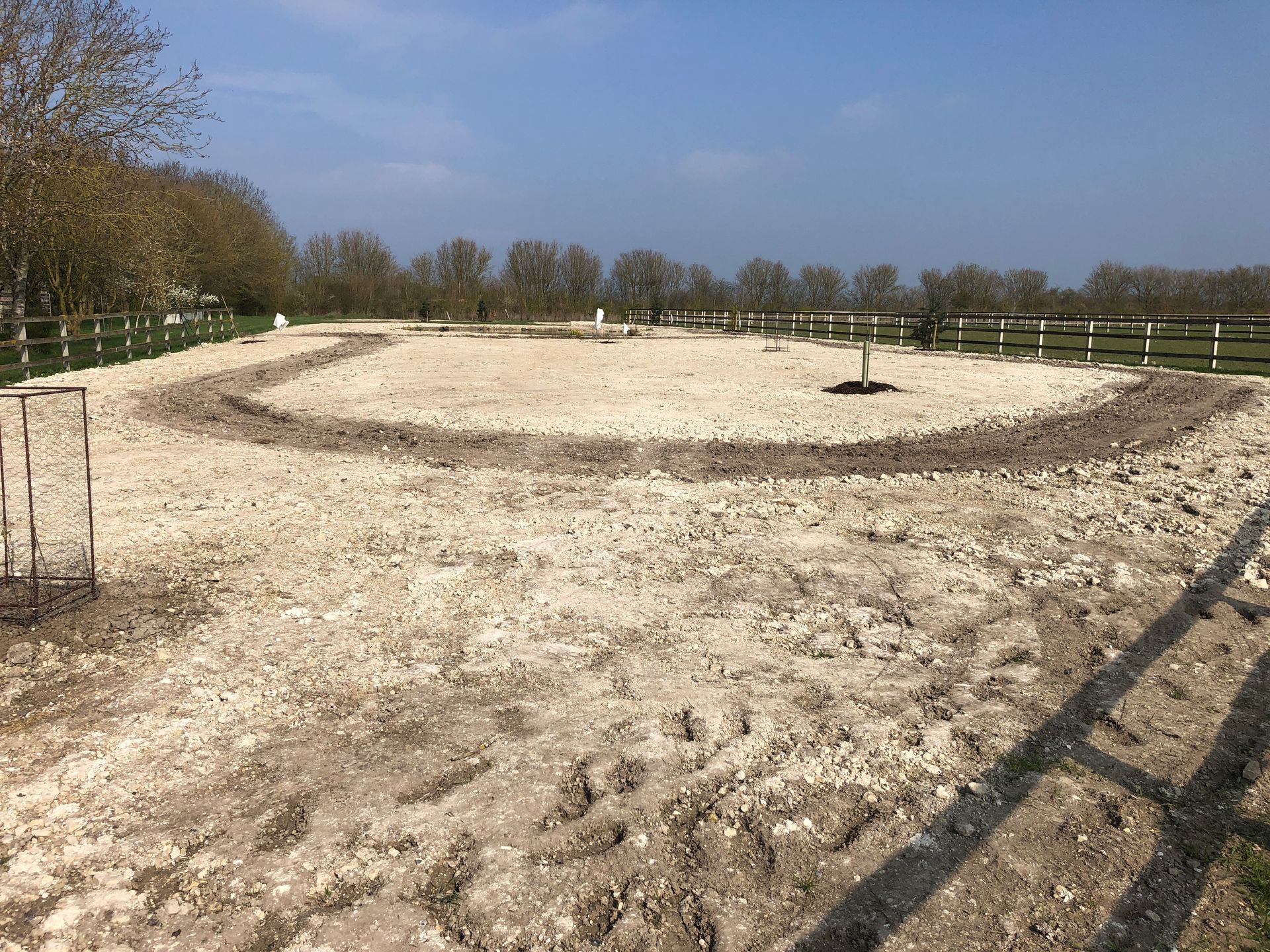 A dirt field with a fence and trees in the background.