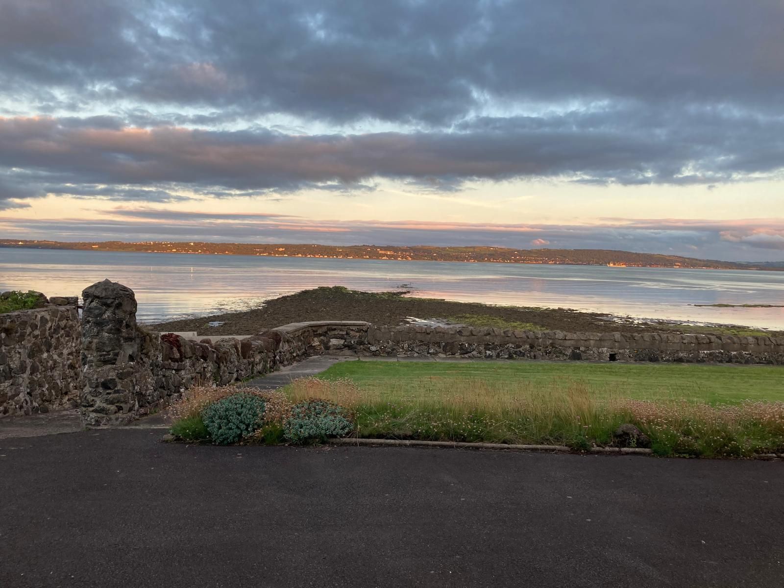 A sunset over a body of water with a stone wall in the foreground.