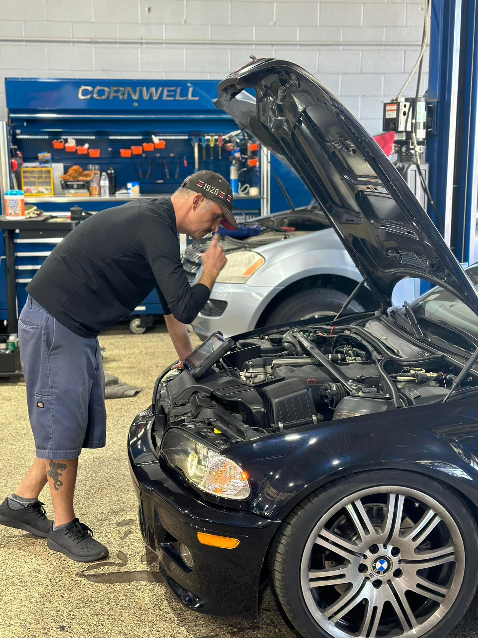 Mechanic inspecting a black BMW engine in a garage with a Cornwell tool cabinet.