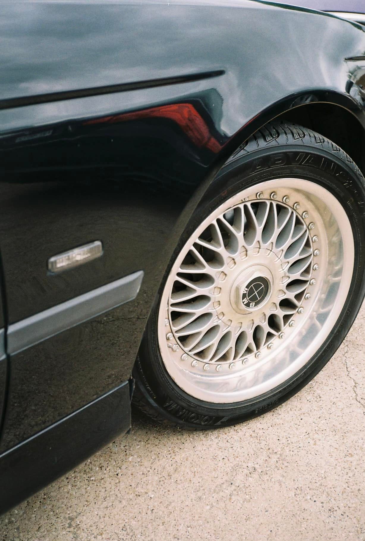Black car's front with a silver spoke wheel. Road setting with side marker light visible.