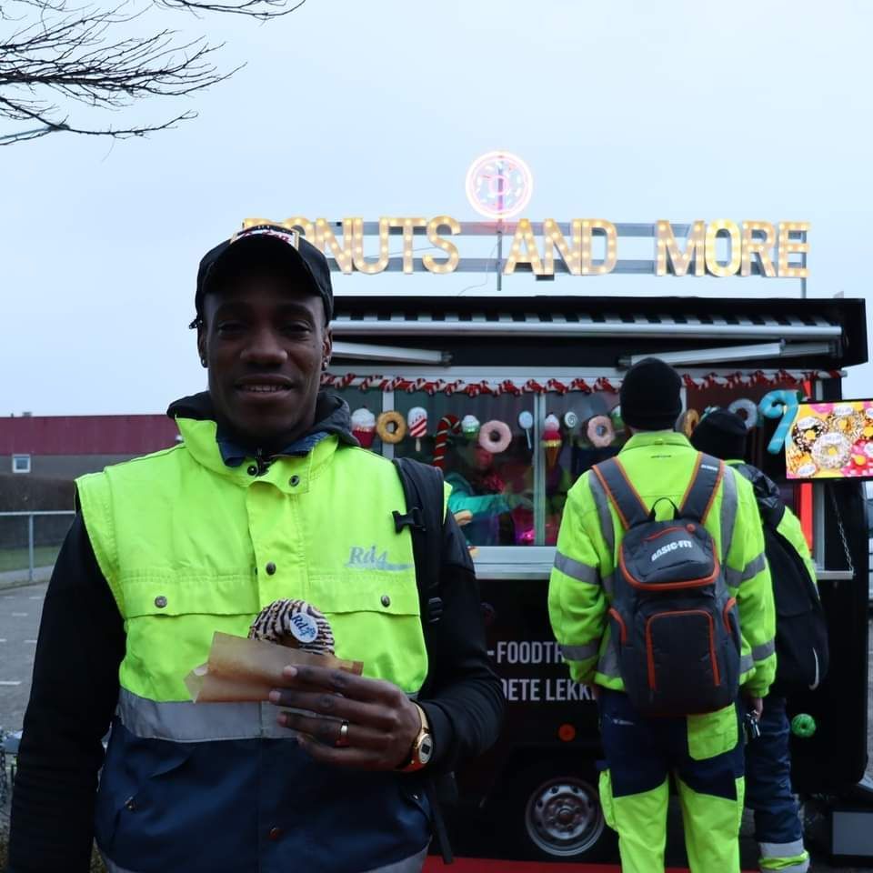 Een man die een donut vasthoudt voor een bord waarop staat 'noten en meer'