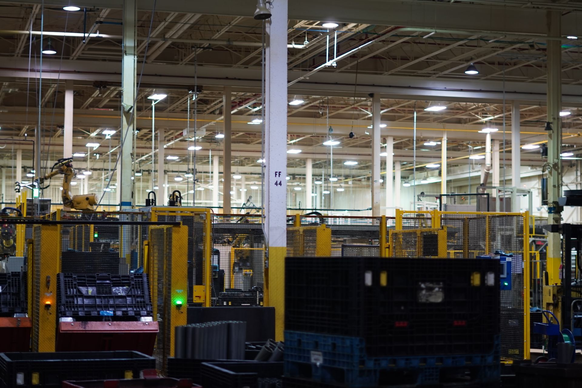 Man on a step stool installs a chandelier in a white room. He wears a tool belt and denim shirt.