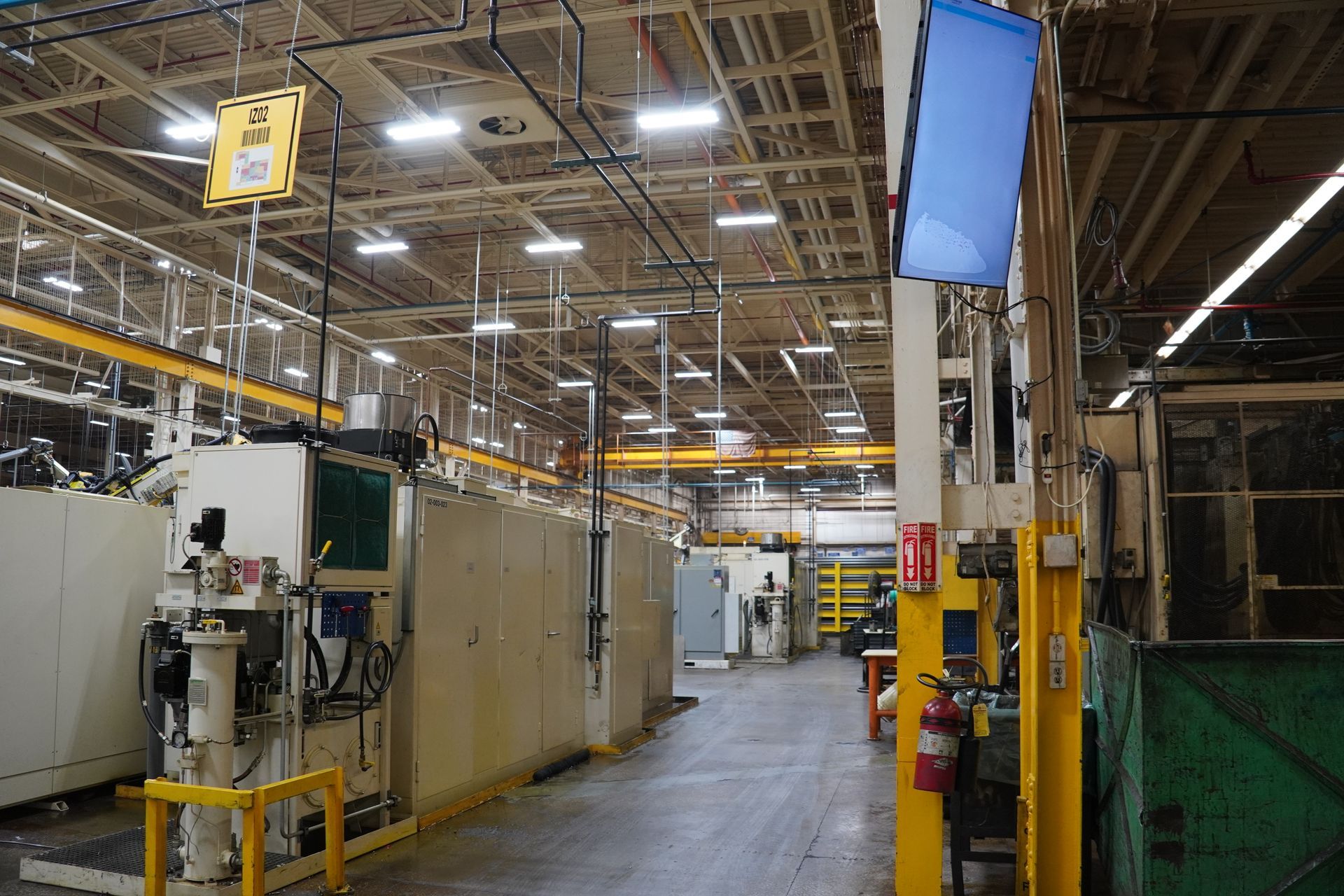 Woman in orange sweater smiles at the camera while holding a phone, sitting at a desk with a computer.