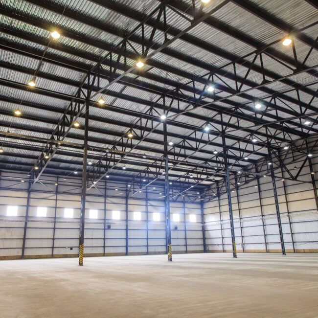 Interior of a large, empty warehouse with metal beams and corrugated ceiling.