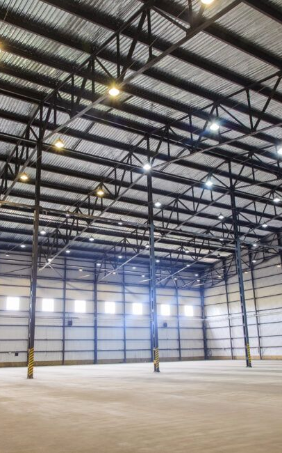 Empty industrial warehouse interior, tall steel columns and beams support a high ceiling with lights.