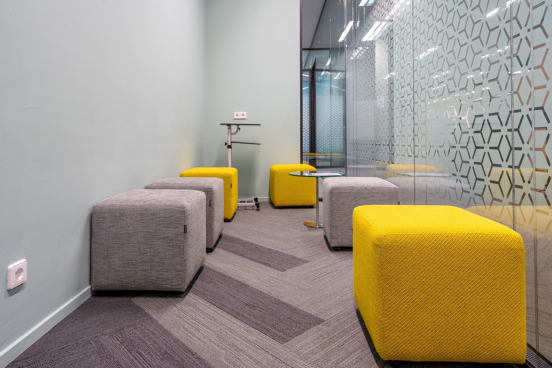 Room with gray and yellow cube-shaped seating, patterned carpet, and frosted glass wall.