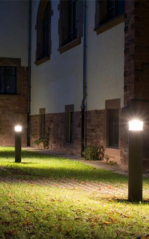 Two illuminated bollard lights on a grassy area in front of a building at night.