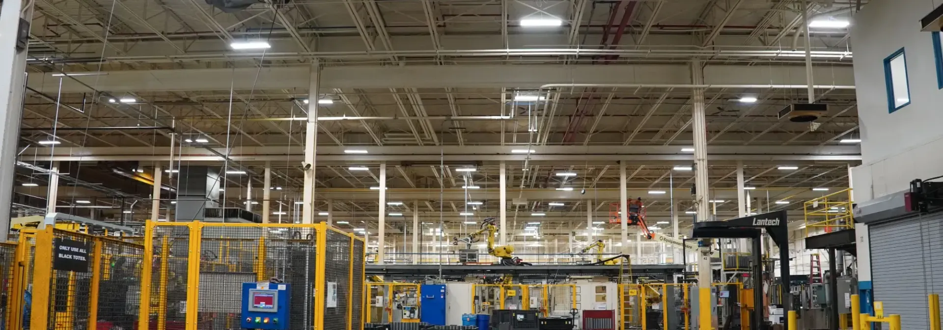 A large, industrial interior with high ceilings and metal infrastructure, and yellow safety structures.