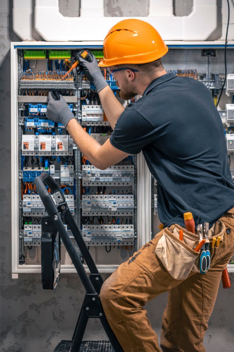 Electrician in orange helmet working on electrical panel, using tools.