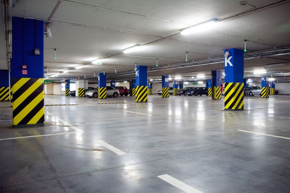 Empty, brightly lit underground parking garage with blue and yellow columns, cars, and directional lines.