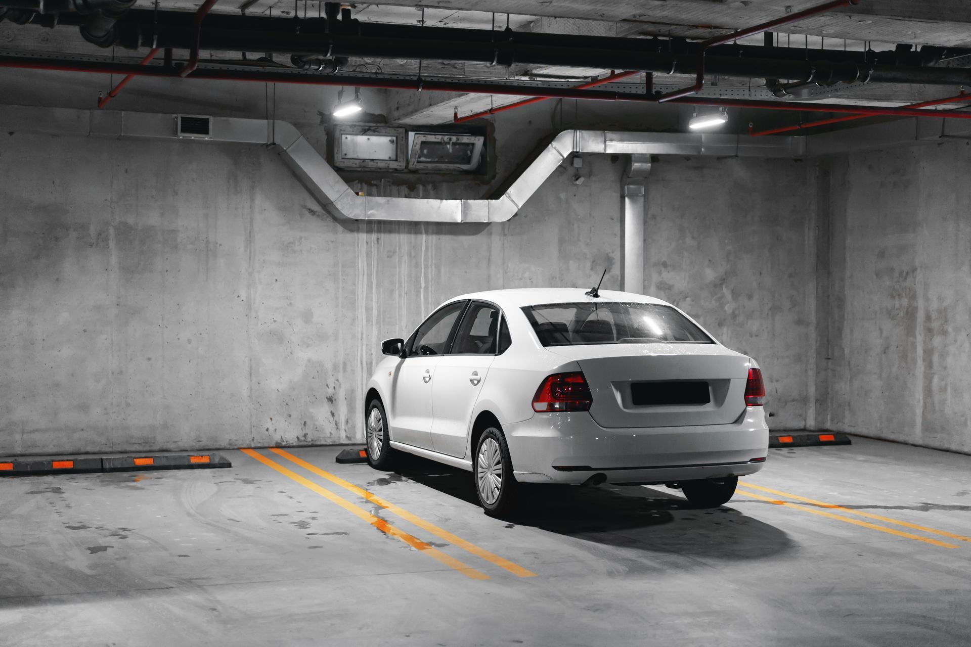 White car parked in an underground parking garage with concrete walls and ceiling.