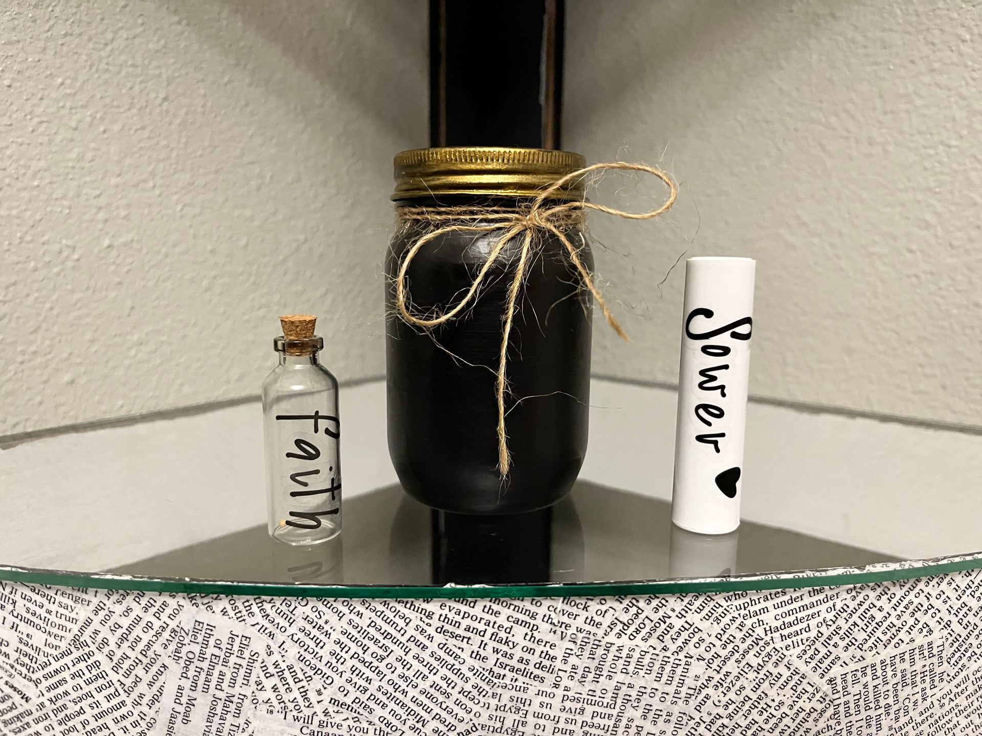 Three small labeled bottles with black, gold, and white decorations on a glass shelf