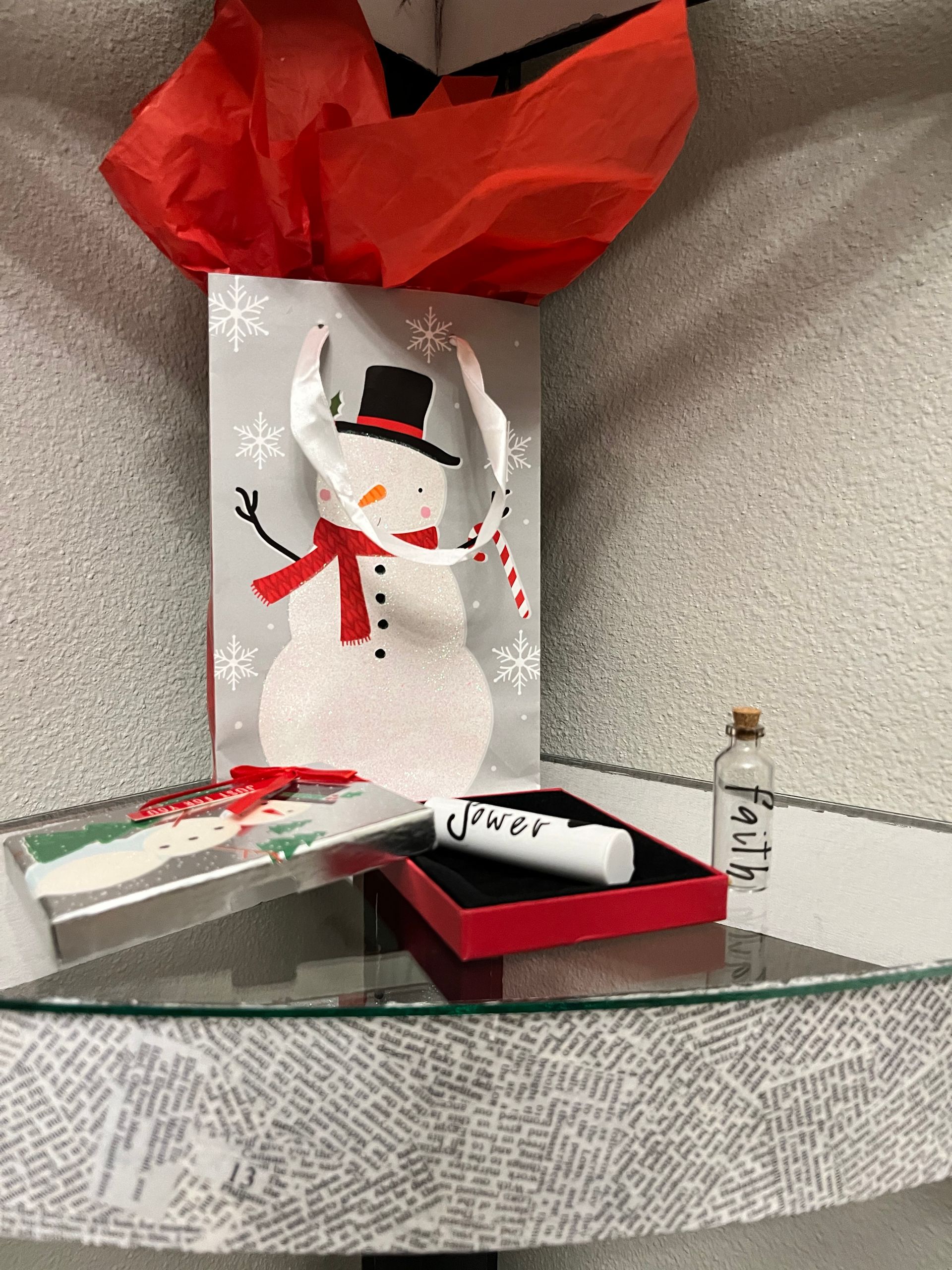 Festive holiday display with snowman decoration, red ribbon, and small gift boxes on a curved tabletop