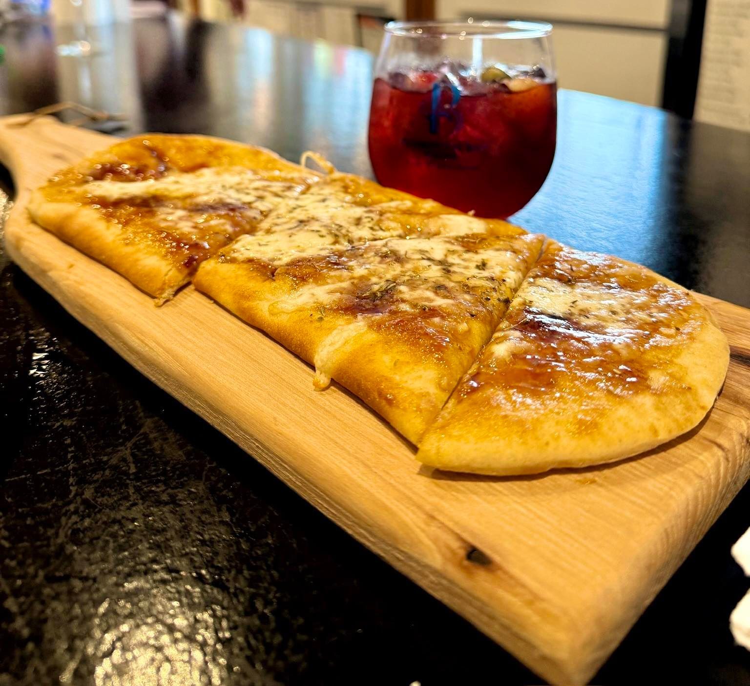 Flatbread on wooden board with drink in glass.