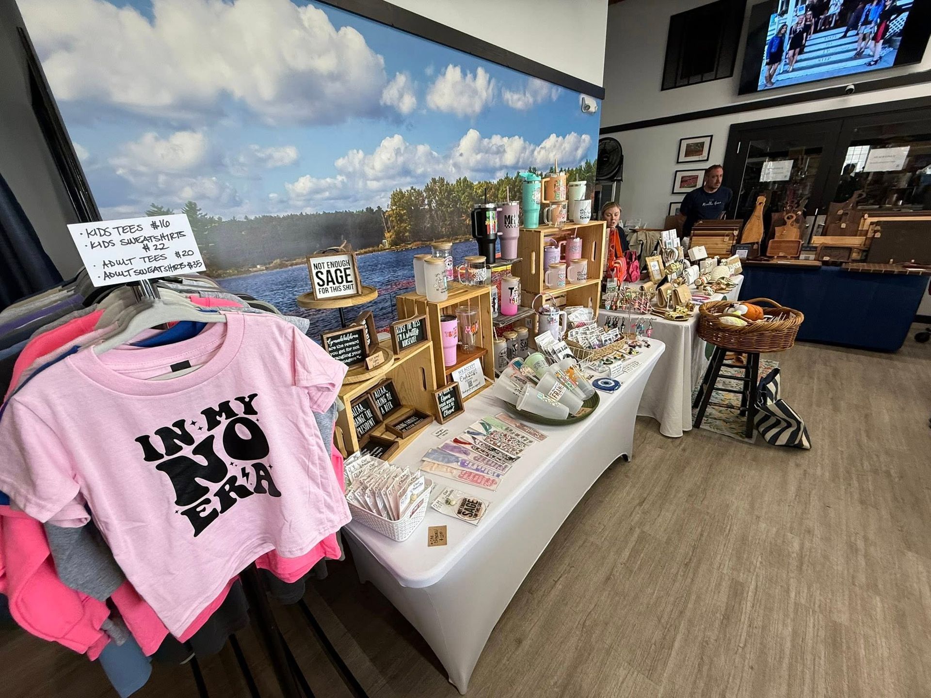 Vendor booth with shirts, tumblers, and crafts displayed in front of a blue sky backdrop.