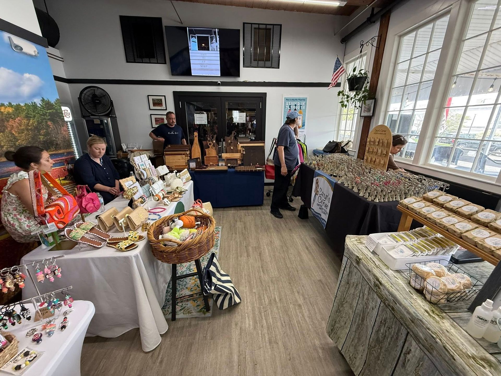 Indoor craft fair with vendors displaying goods on tables; people browse and shop.