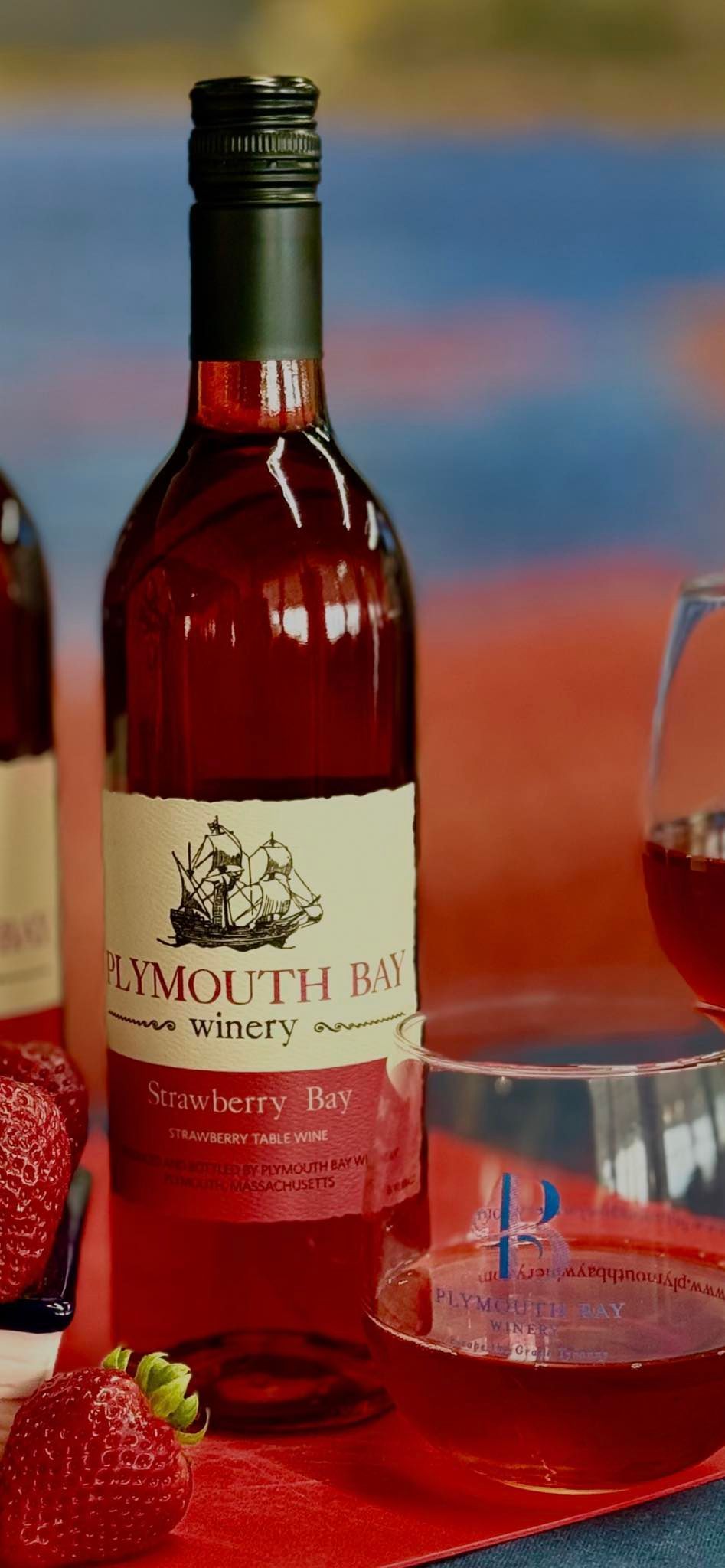 Bottle of red wine with a label, glass of wine, strawberries on red background.