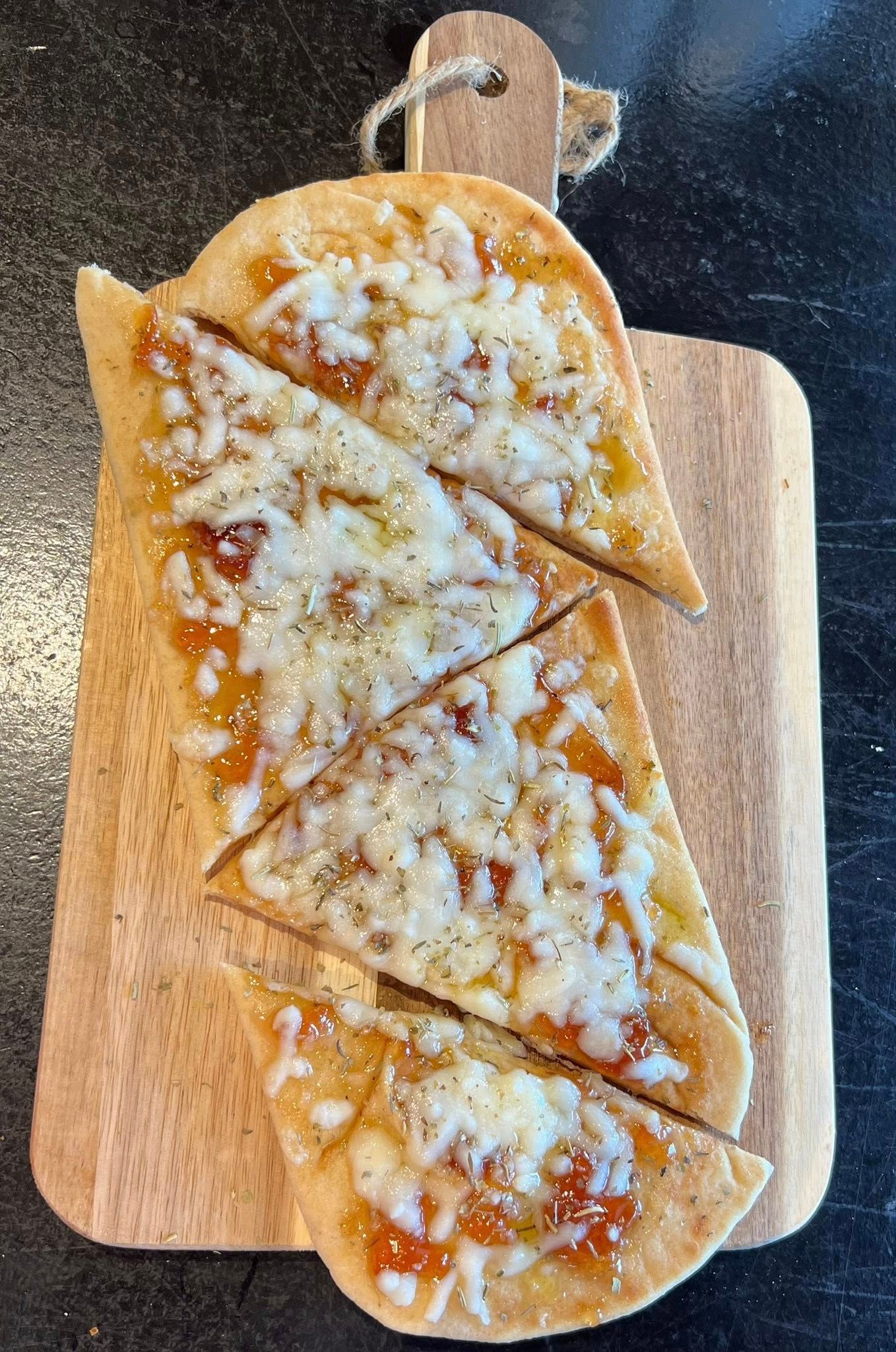 Flatbread pizza on a wooden cutting board, sliced into triangles, topped with cheese.