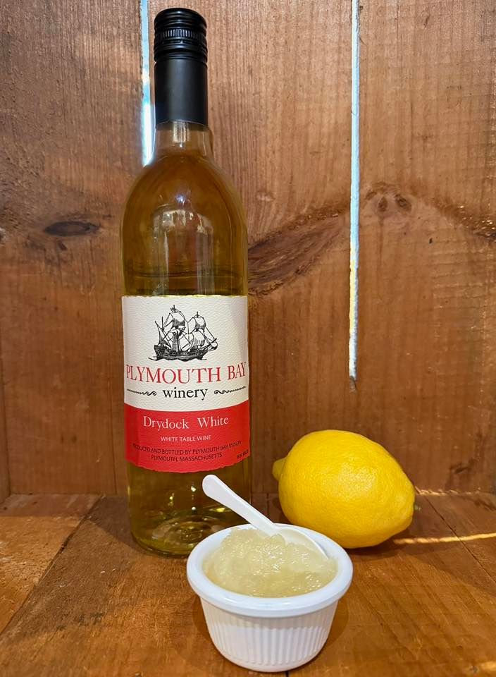 Plymouth Bay white wine bottle, small cup of sauce, and a lemon on wooden surface.