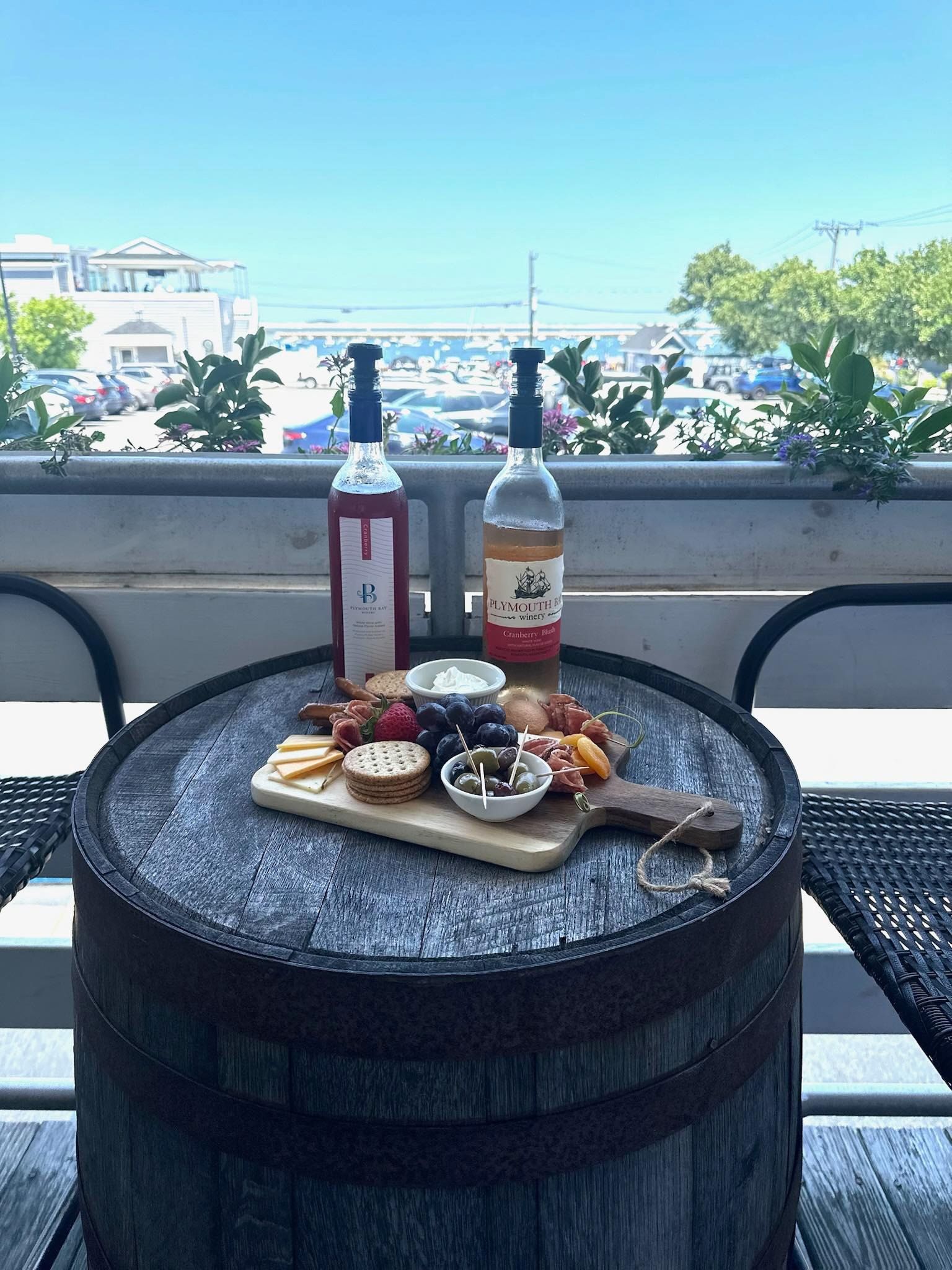 Wine bottles and charcuterie board on a barrel table, outdoor setting with a view.