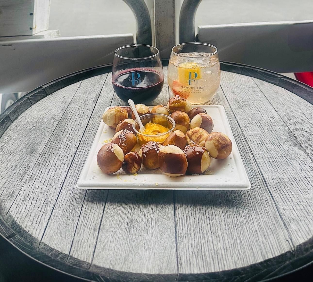 Pretzel bites with dipping sauce and drinks on a wooden barrel table.