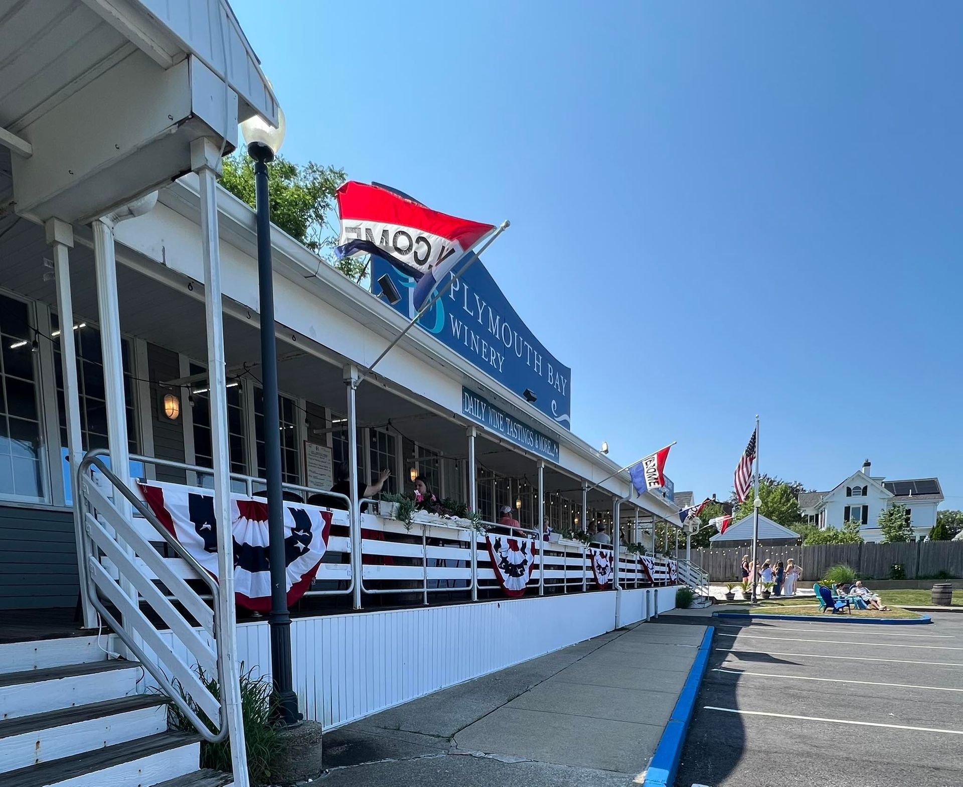 A long white building with blue lettering, decorated with patriotic bunting and flags on a sunny day.