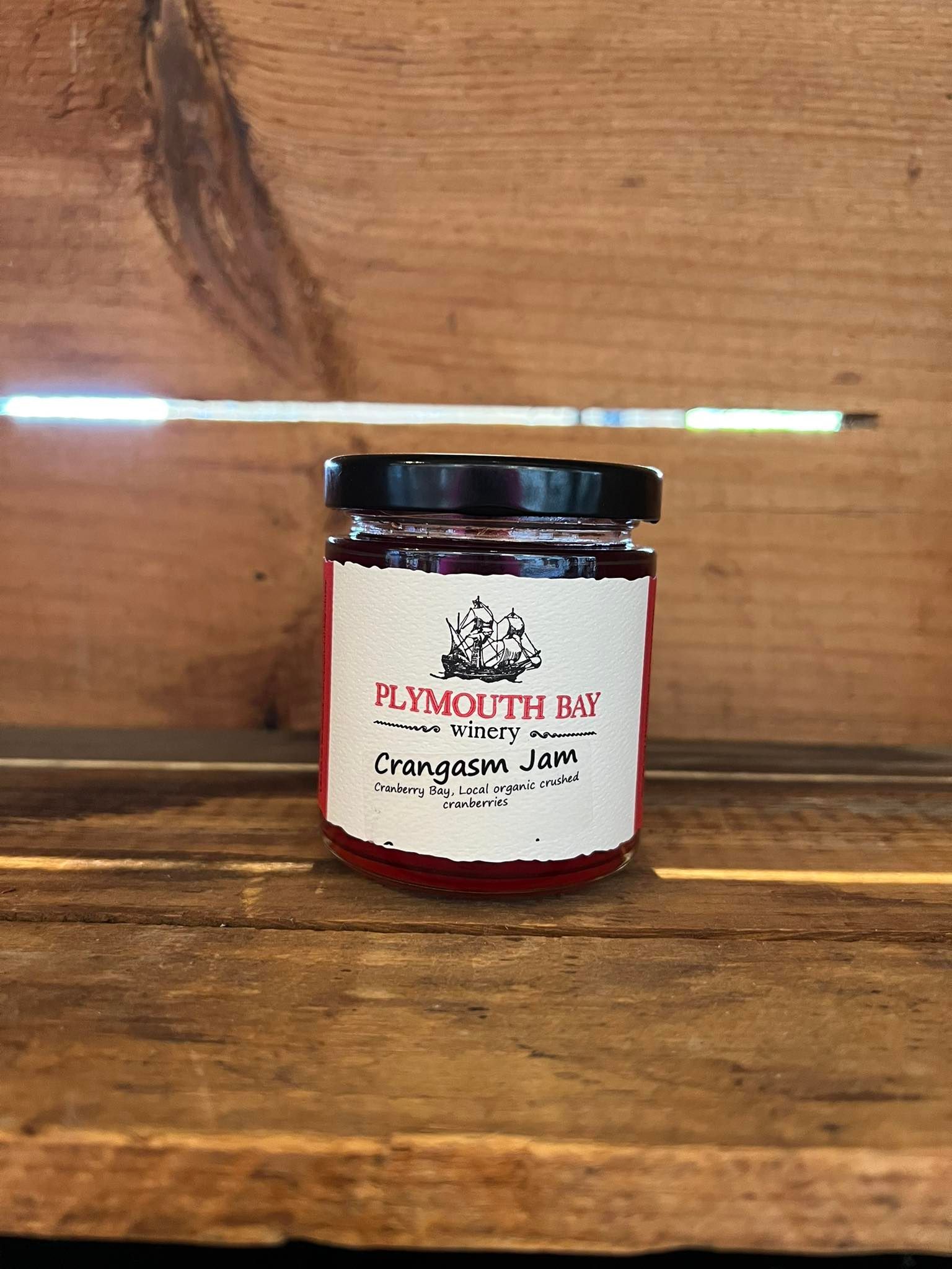 Jar of Plymouth Bay Cranberry Jam on wooden surface.