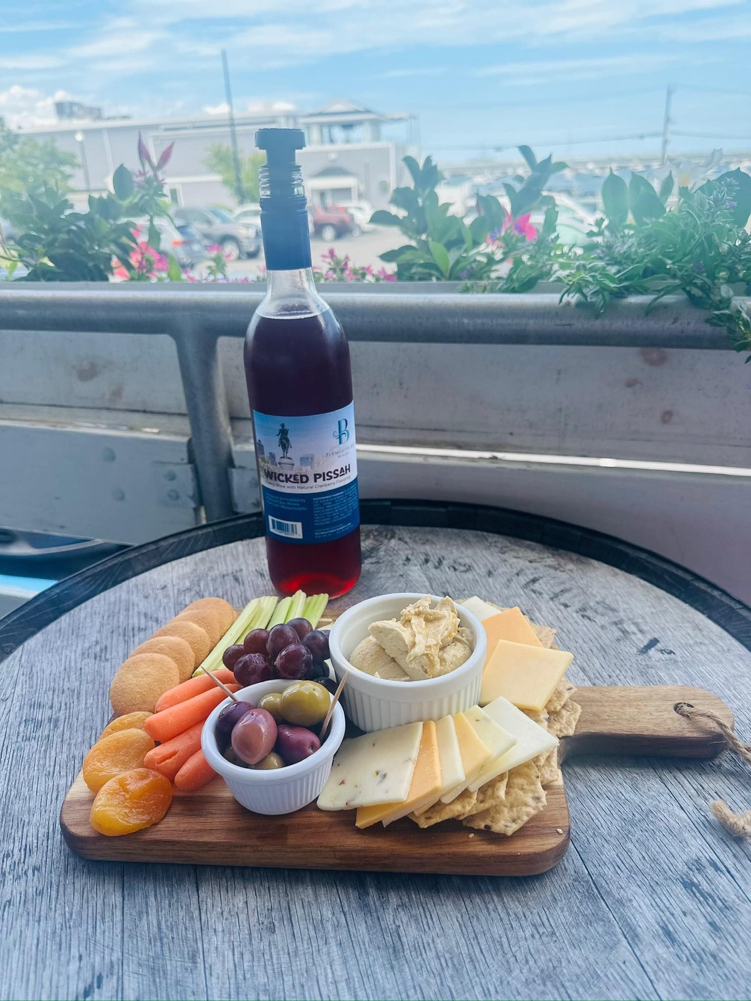 Charcuterie board with hummus, cheese, crackers, and wine bottle on a table with an outdoor background.