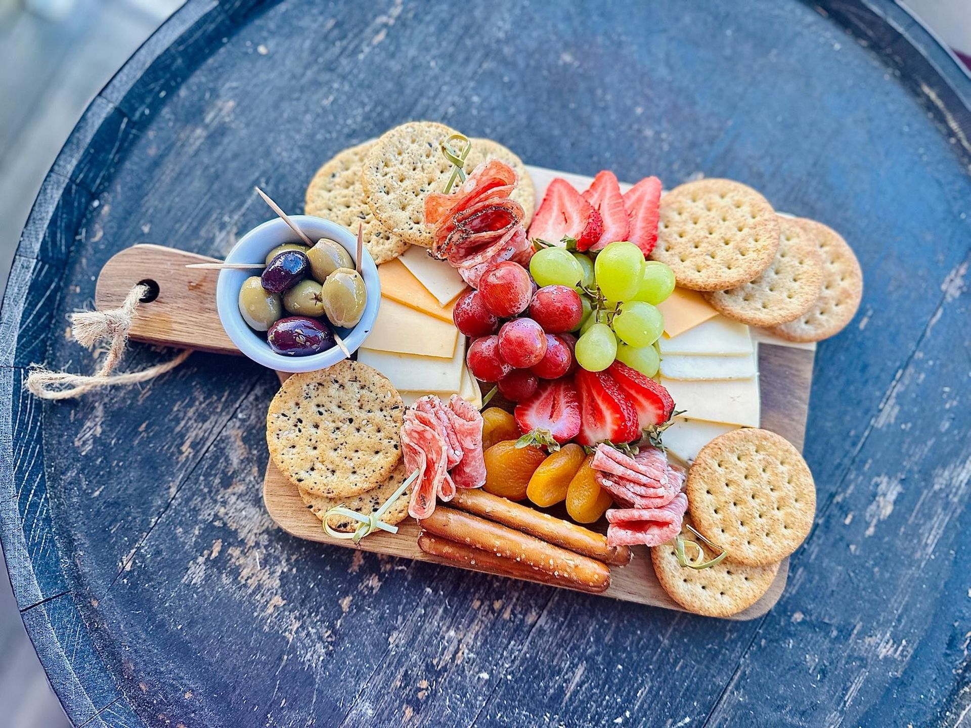Charcuterie board: cheese, crackers, grapes, strawberries, olives, prosciutto, and apricots on wooden platter.