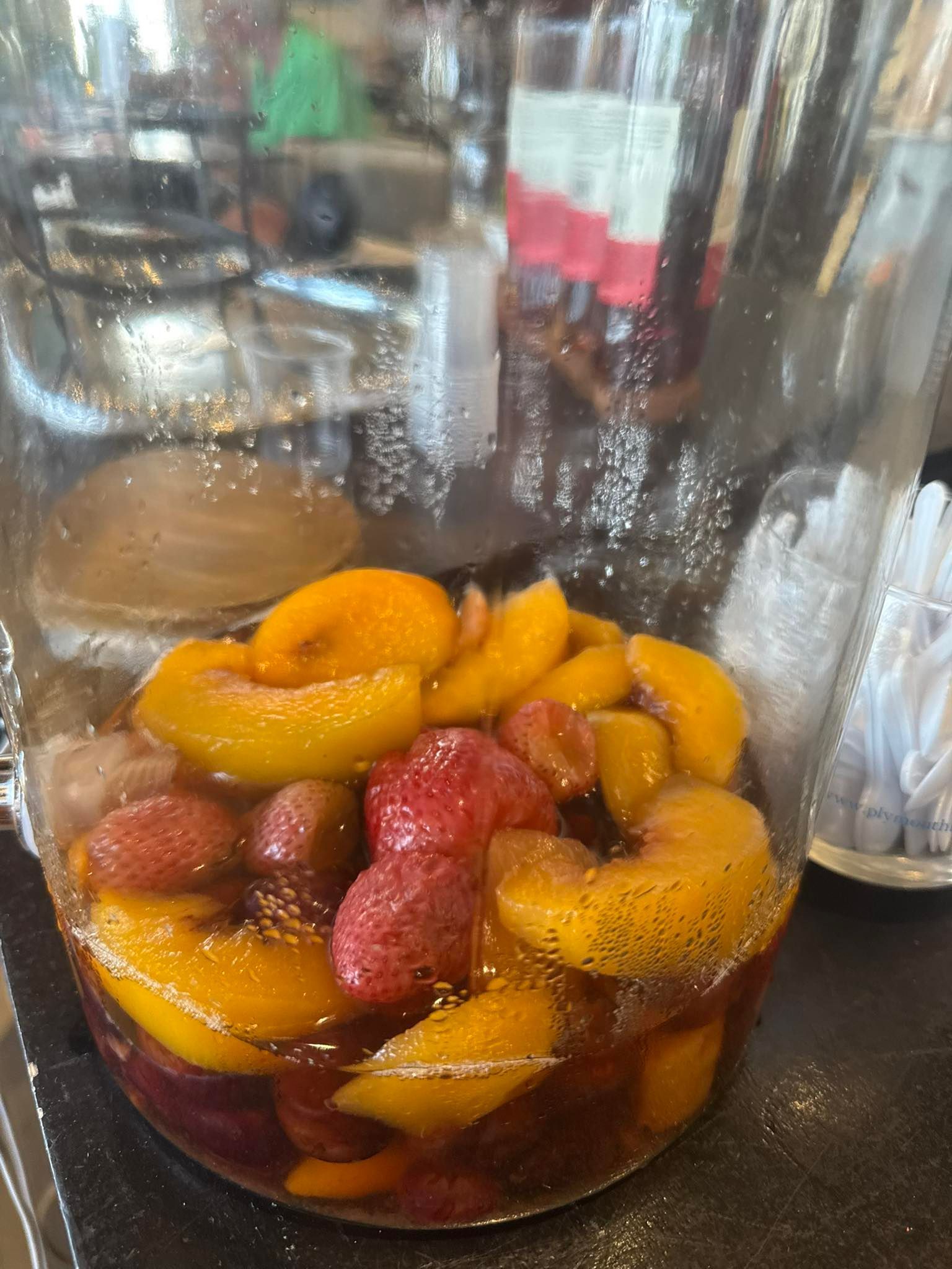 Glass pitcher with sliced peaches and red fruit, bubbling in a dark liquid.