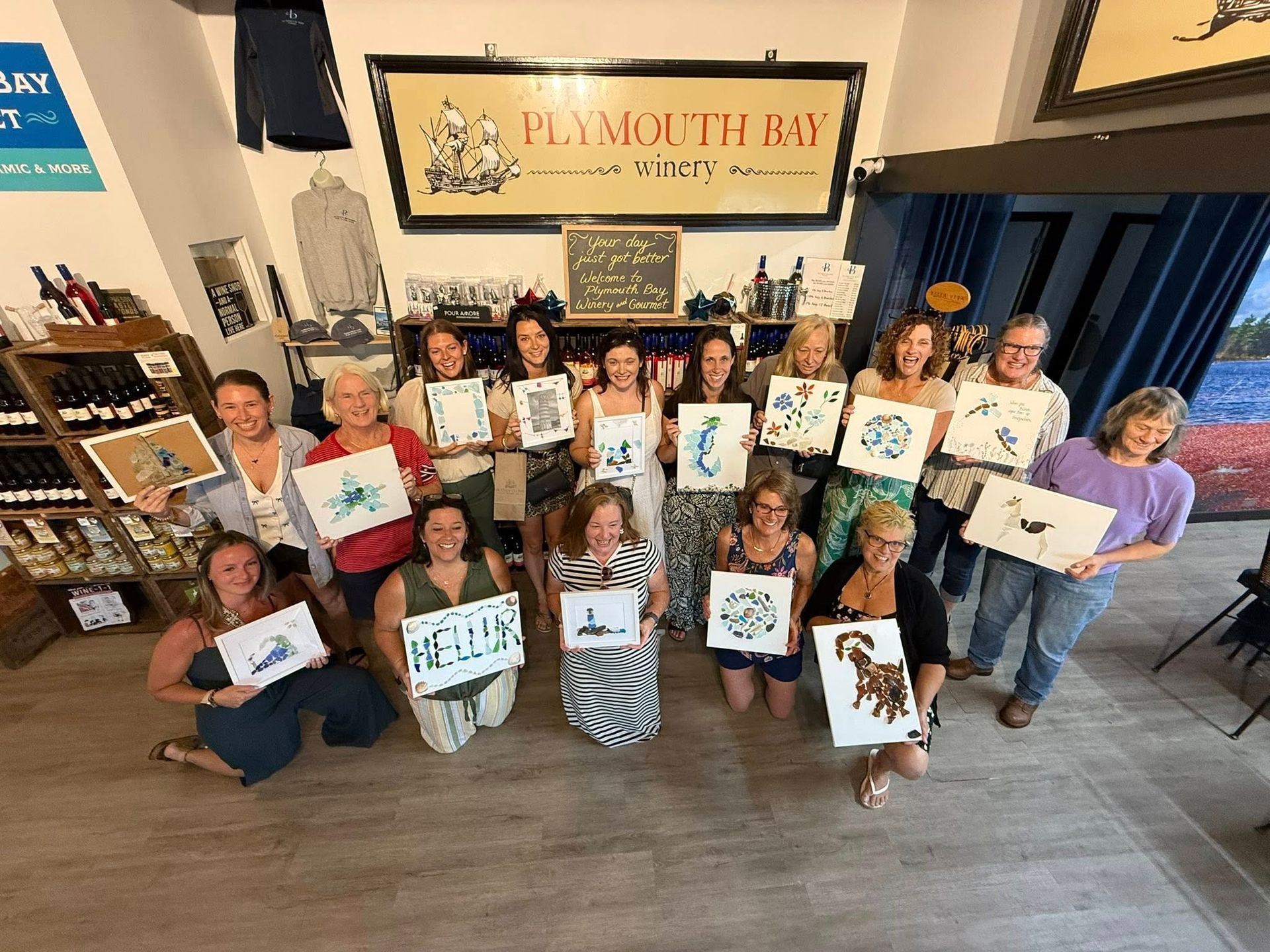 Group of women in a shop hold up paintings. 