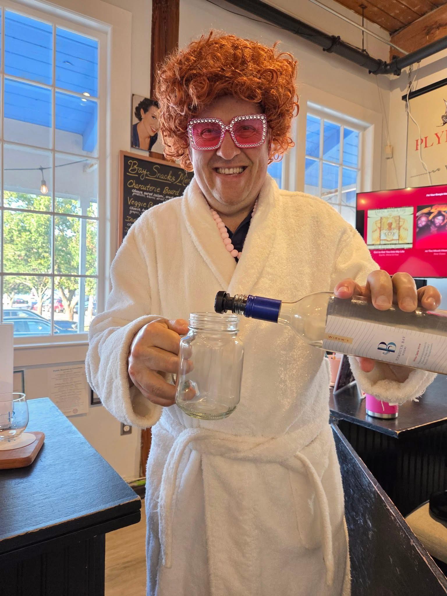 Man in robe and wig pouring drink into a jar at a bar.