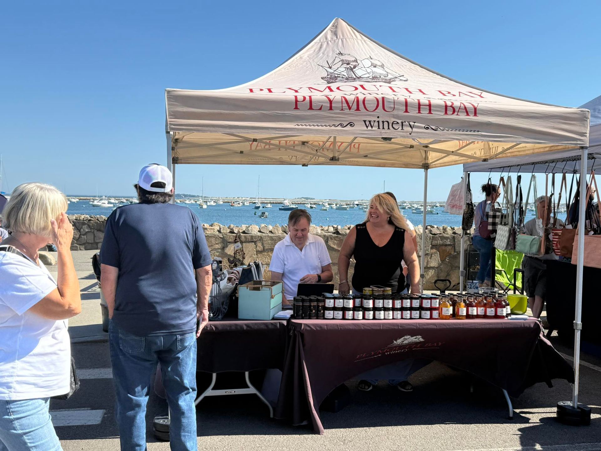 People at a Plymouth Bay Winery market tent, with ocean view.