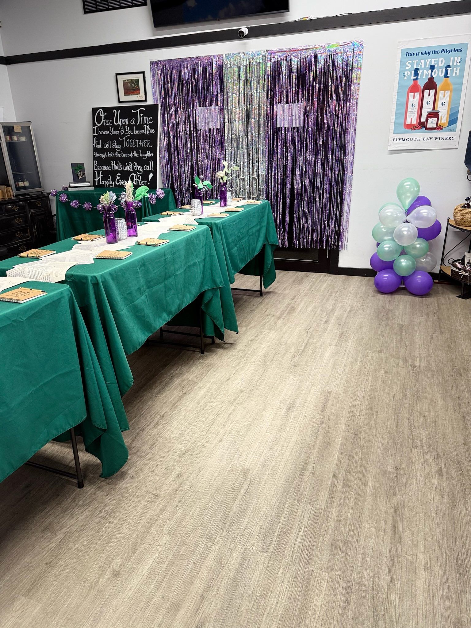 Long table with green tablecloths, set for a gathering. Balloons and purple decor.