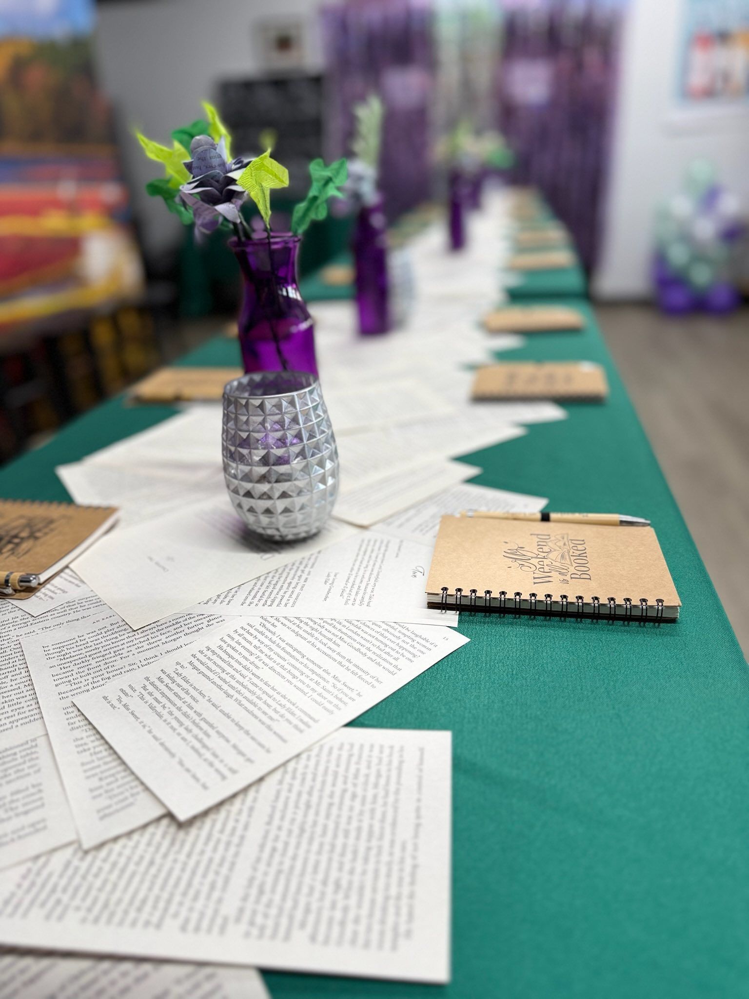 Long table set with floral decorations, papers, and notebooks on a green tablecloth.