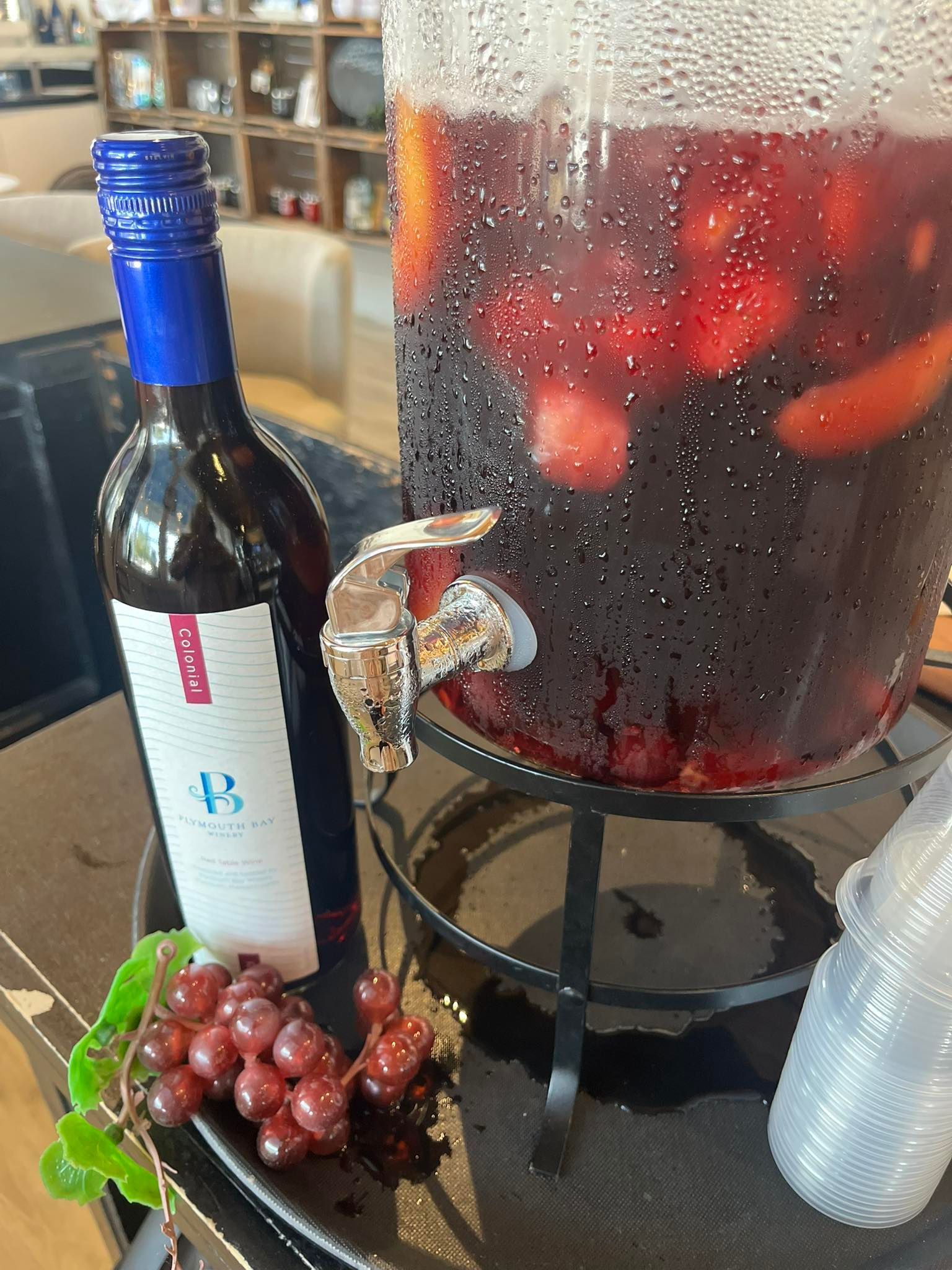 Wine bottle, sangria dispenser, and grapes on a tray.