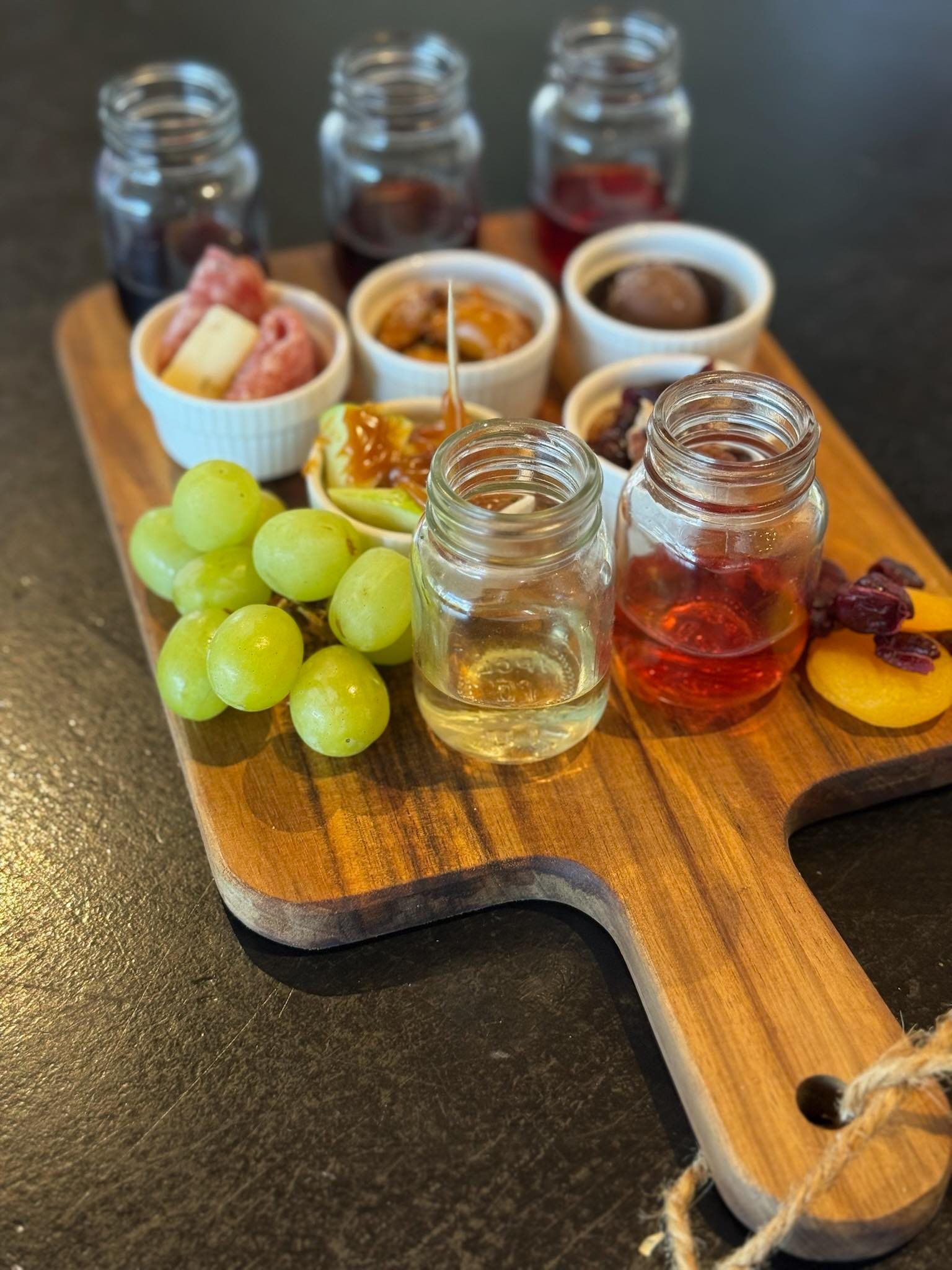 Charcuterie board with jars of sauces, small bowls of food, grapes, and a peach.