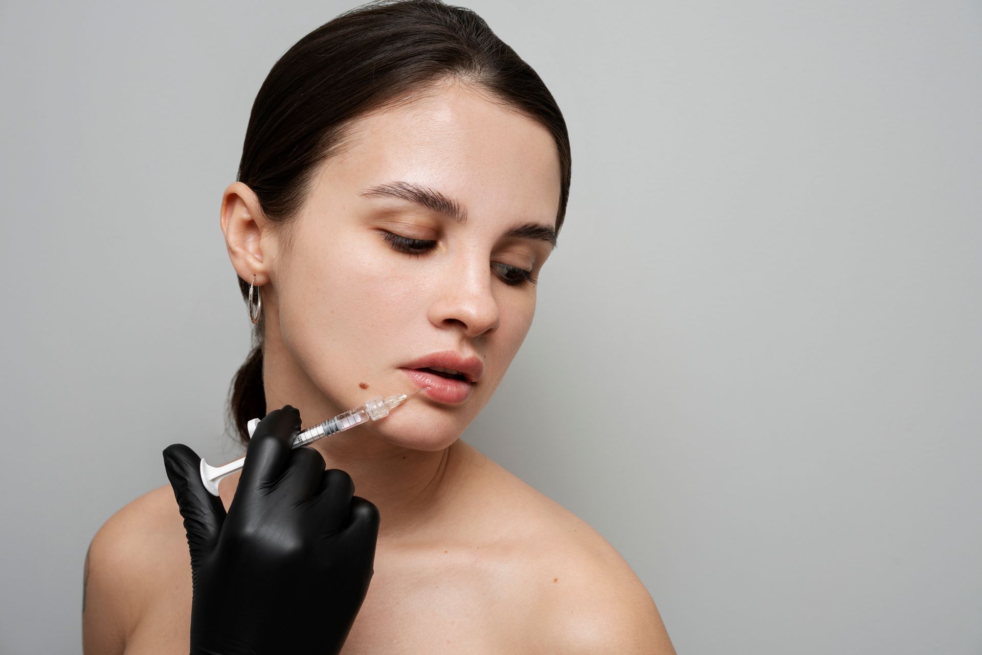 Woman receiving lip injection, gloved hand holding syringe.