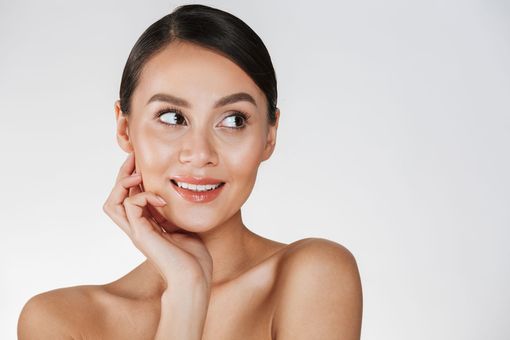 A woman is smiling and touching her face with her hands.