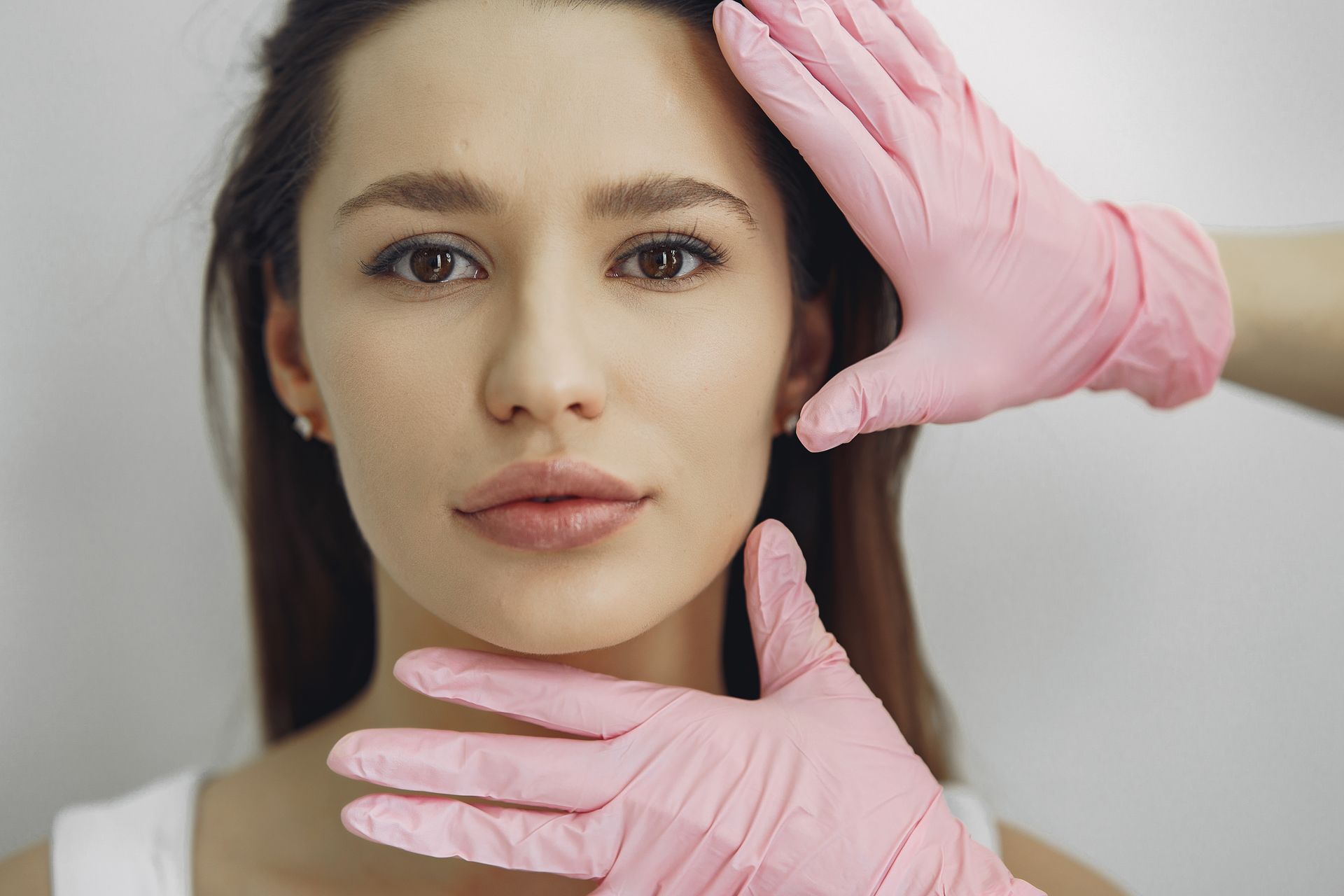 A woman wearing pink gloves is covering her face with her hands.